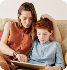 A mother teaching her son on tablet while sitting on the couch.