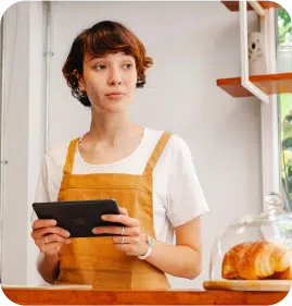 A standing woman in her kitchen ordering food from her tablet.